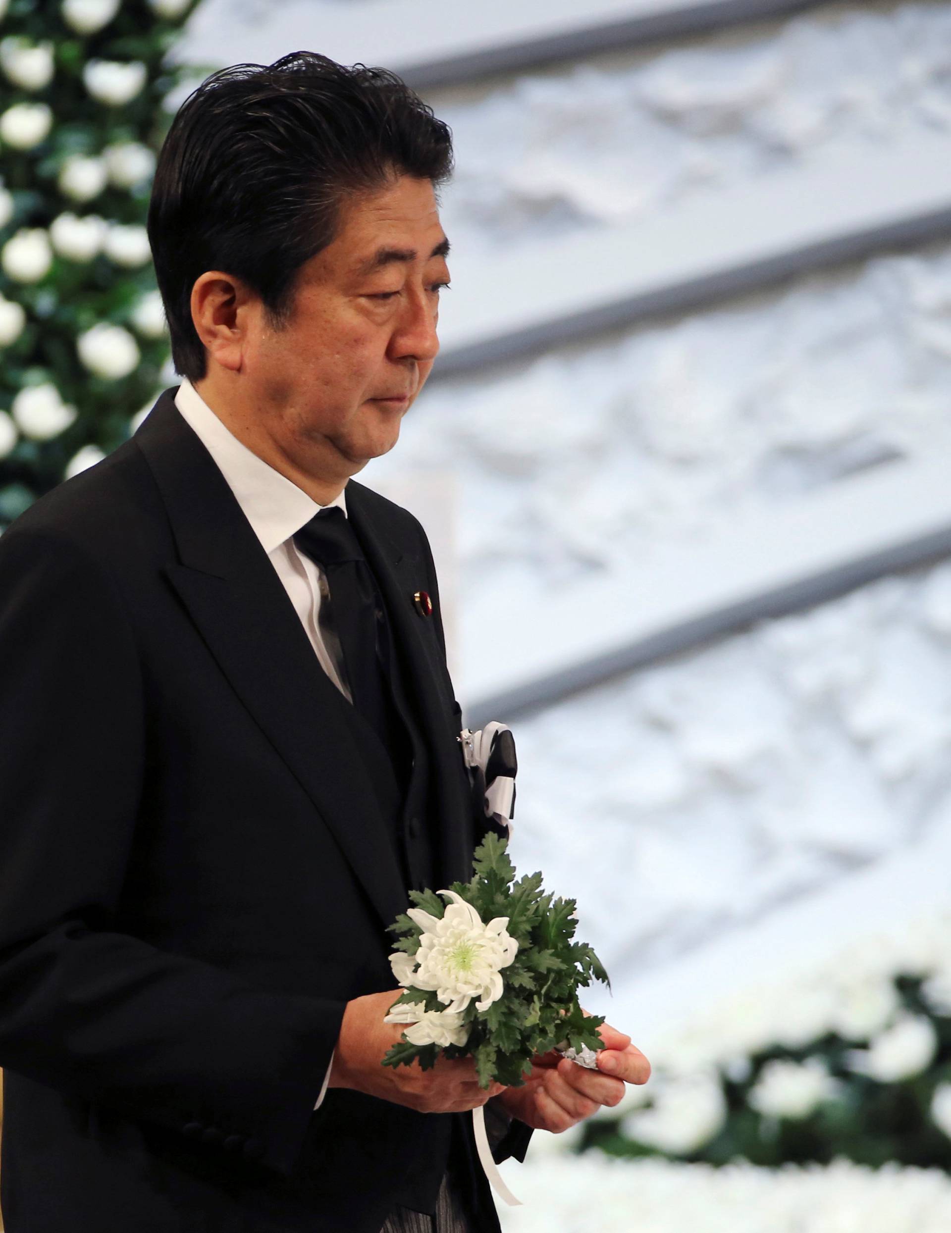 Japanese Prime Minister Shinzo Abe holds a chrysanthemum to offer for the victims of the March 11, 2011 earthquake and tsunami during the national memorial service in Tokyo