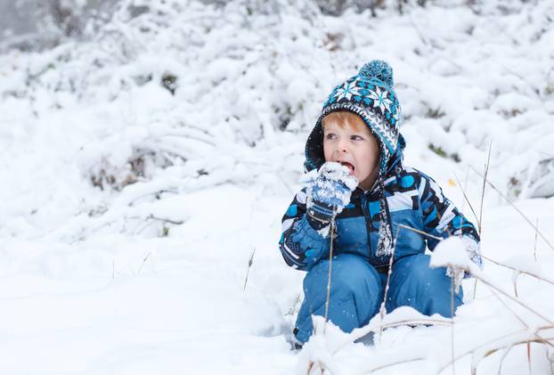 Adorable toddler boy having fun with snow on winter day 