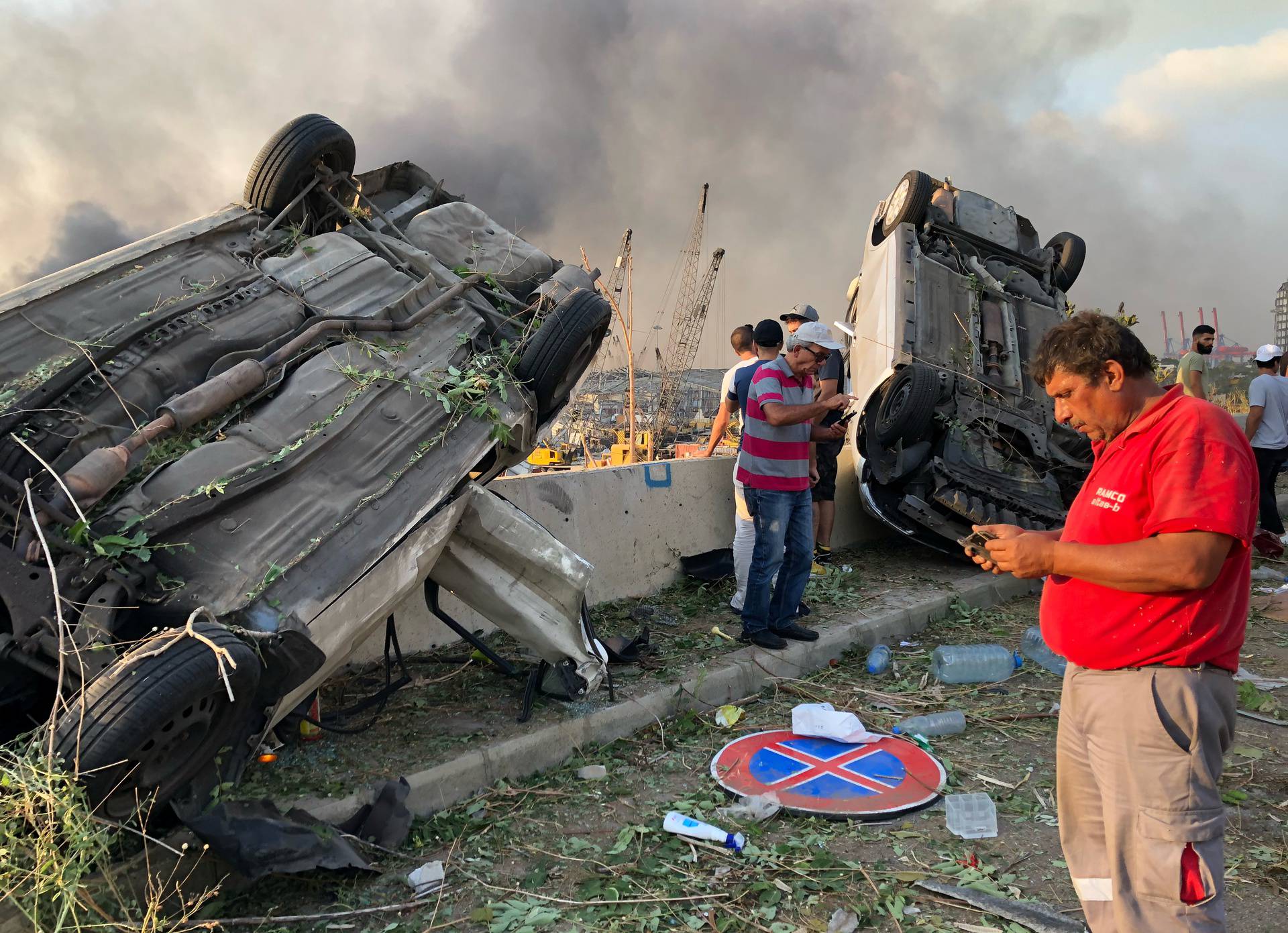 People stand near damaged cars following an explosion in Beirut