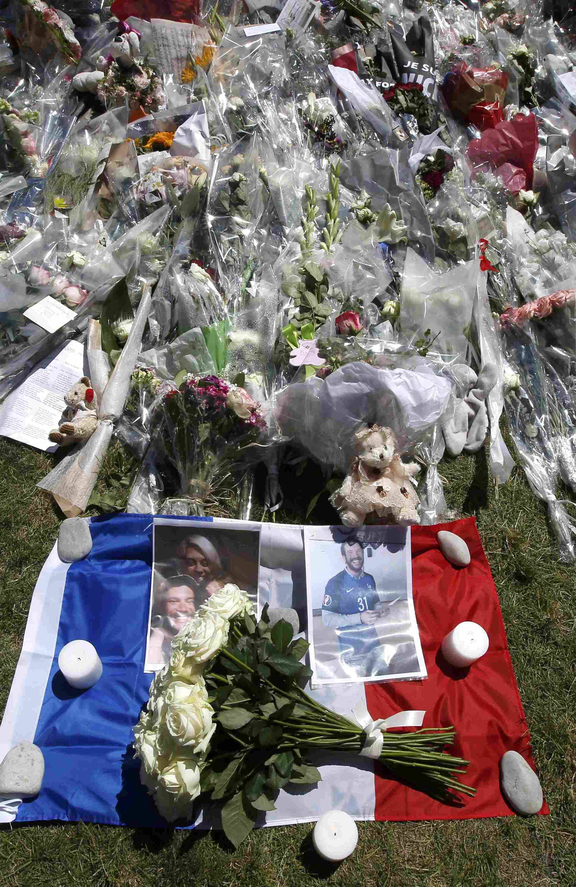 Pictures are seen on a French flag near tributes of flowers two days after an attack by the driver of a heavy truck who ran into a crowd on Bastille Day killing scores and injuring as many on the Promenade des Anglais, in Nice