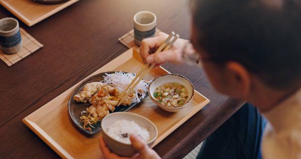 Man, hands and eating food with chopsticks at dinner table for meal, snack or cuisine at home. Closeup, Japan or male person tasting with bowl or utensils for dining culture, tradition or heritage