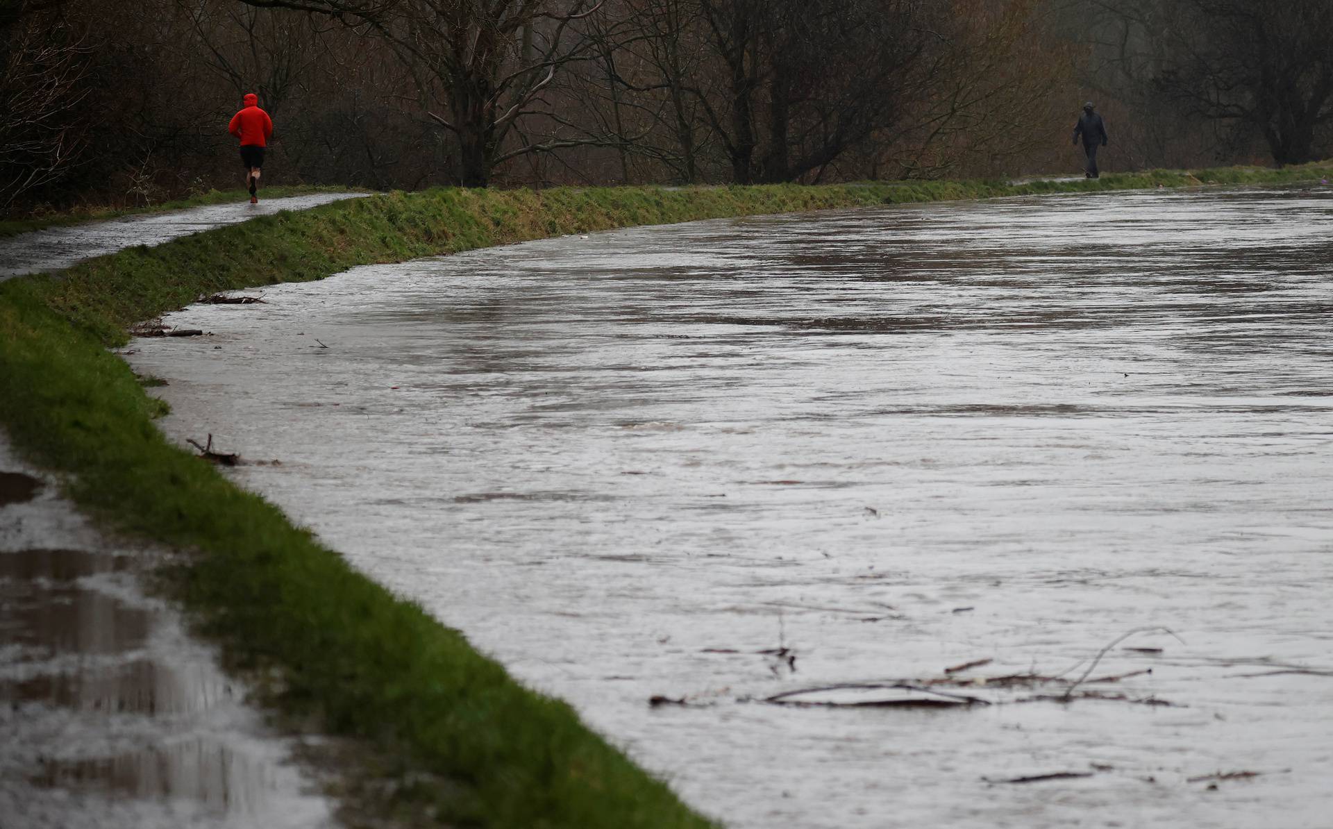 People exercise along the banks of a heavily flooded River Mersey as Storm Christoph arrives in Manchester