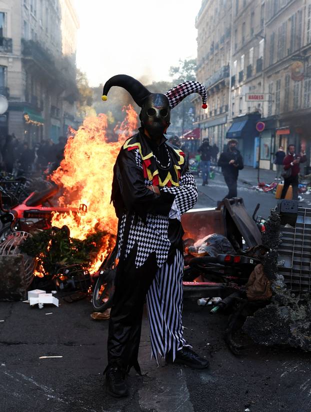 A demonstrator wearing a costume stands in front of burning flames, in Paris