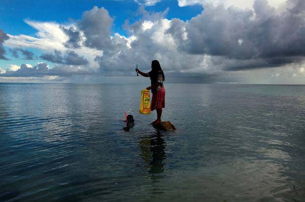 FILE PHOTO: Binata Pinata stands on top of a rock holding a fish her husband Kaibakia just caught on Bikeman Islet, located off South Tarawa in the central Pacific island nation of Kiribati