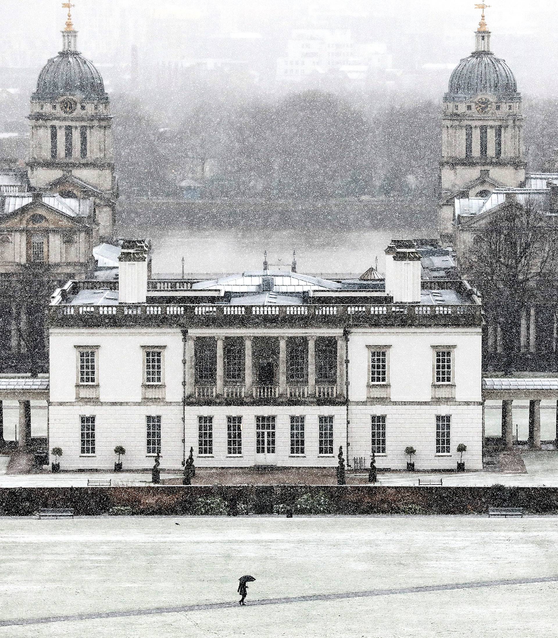 A pedestrian walks through the snow in Greenwich Park, next to National Maritime Museum, London