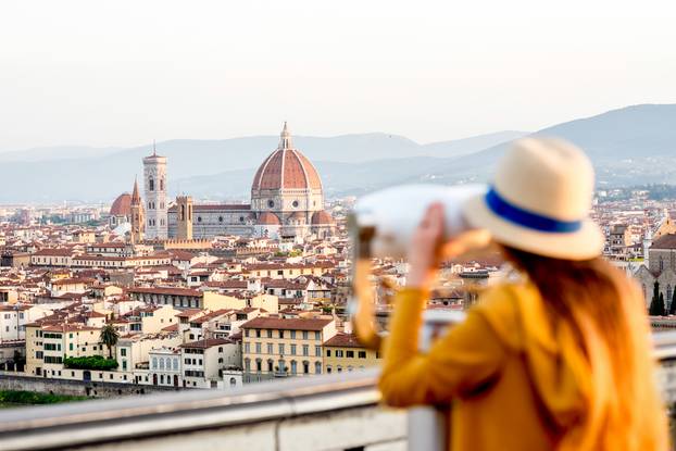 Young,Female,Tourist,Looking,With,Telescope,On,The,Old,Town