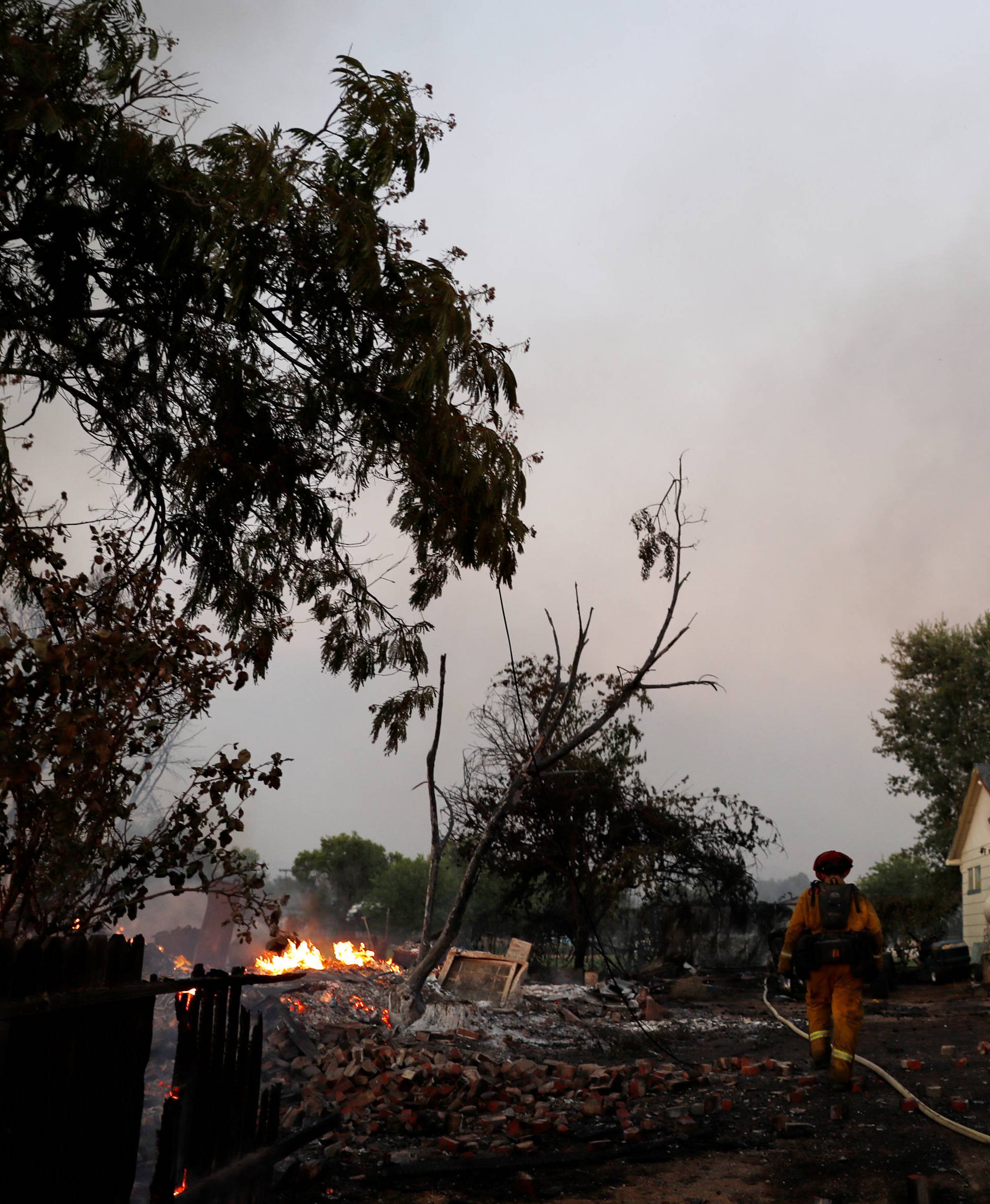 A firefighter carries a hose into a property damaged by the Clayton Fire near Lower Lake in California