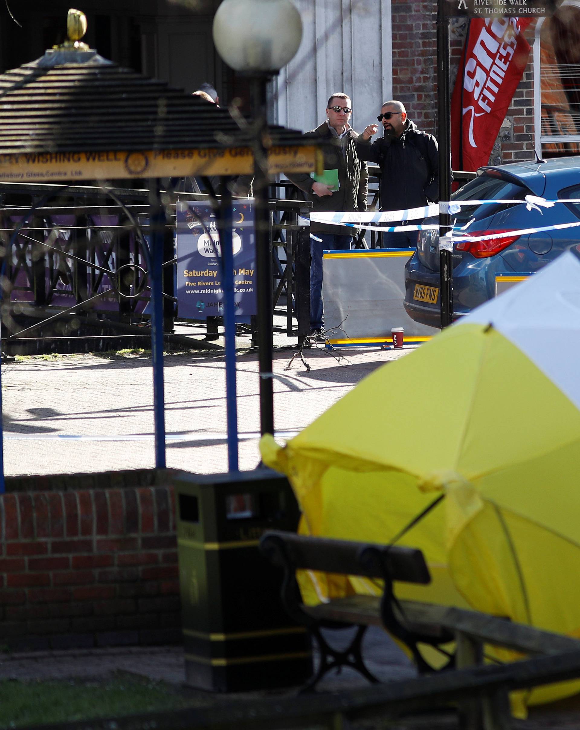Local officials survey the scene as the forensic tent, covering the bench where Sergei Skripal and his daughter Yulia were found, is blown out of position in the centre of Salisbury