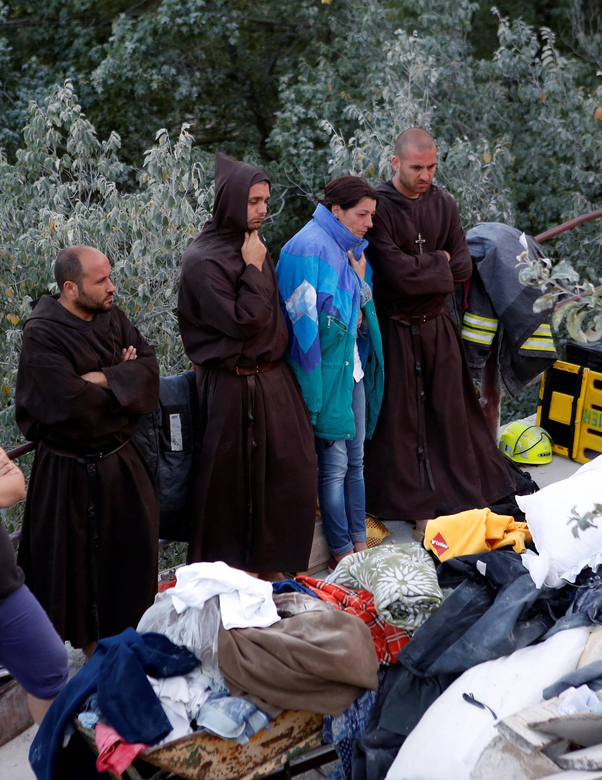 Friars stand with two women in front of collapsed house following an earthquake in Pescara del Tronto