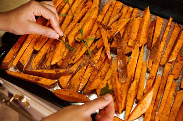 Healthy sweet potato fries on a baking sheet. Delicious vegan meal - roasted batata wedges baked with rosemary leaves