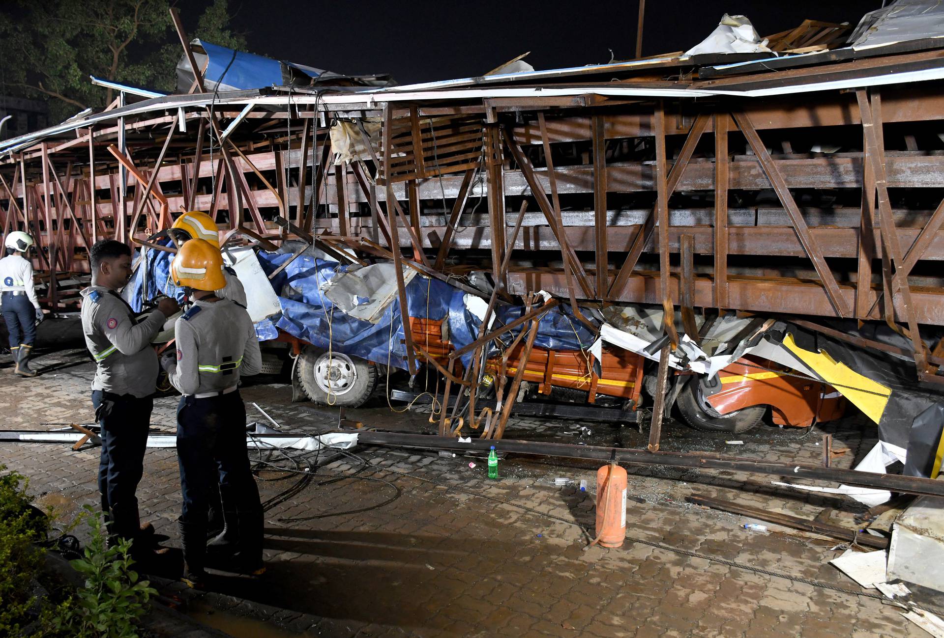 Firefighters stand next to the damaged vehicles trapped in the debris after a massive billboard fell during a rainstorm in Mumbai