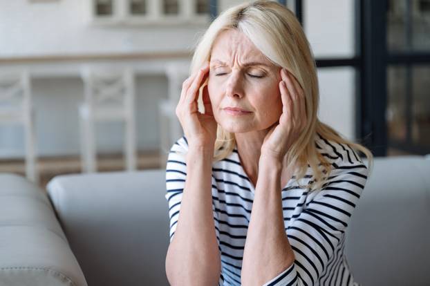 Portrait of mature woman touching temples and have problems with memory,