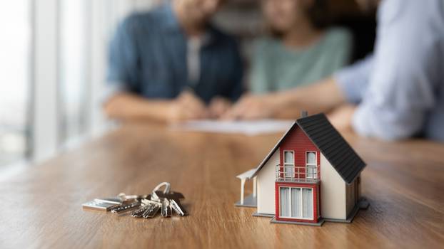 Close,Up,Of,Key,And,Tiny,Toy,House,On,Table.