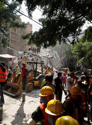 A man motions for everybody to be quiet as rescue workers look for people under the rubble of a collapsed building after an earthquake hit Mexico City, Mexico