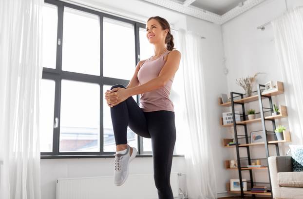 smiling young woman stretching leg at home