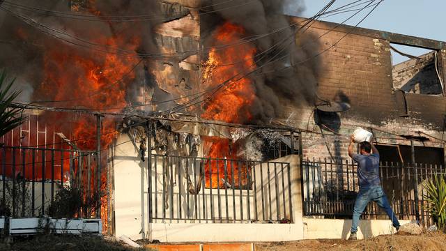 A man tries to extinguish a fire burning a house during the spread of wildfires in Vina del Mar