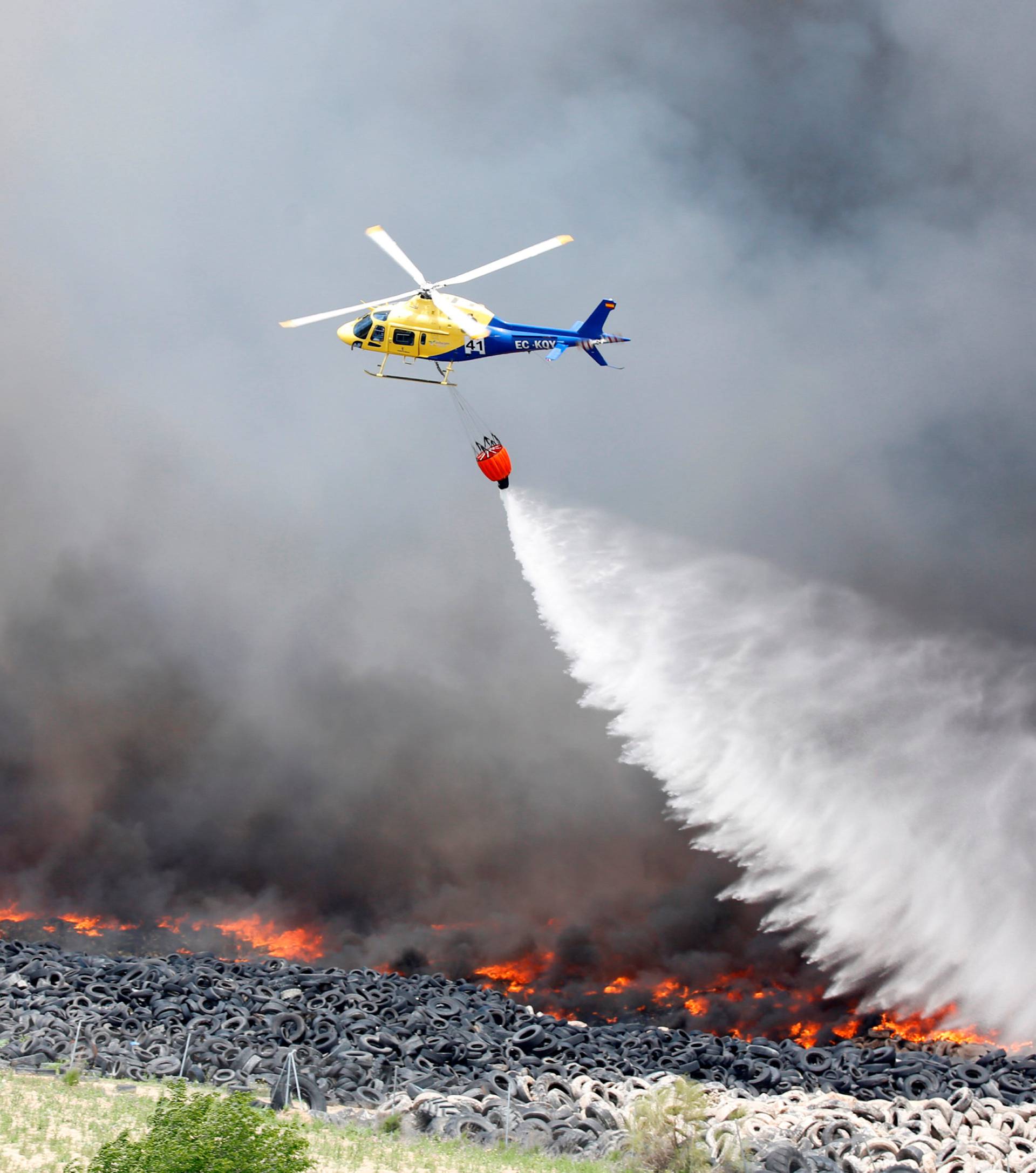 An helicopter throws water over a fire at a tire dump near a residential development in Sesena