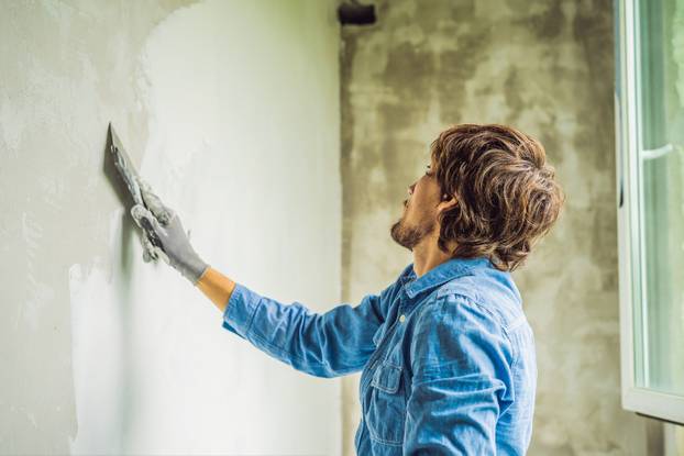 master is applying white putty on a wall and smearing by putty knife in a room of renovating house in daytime