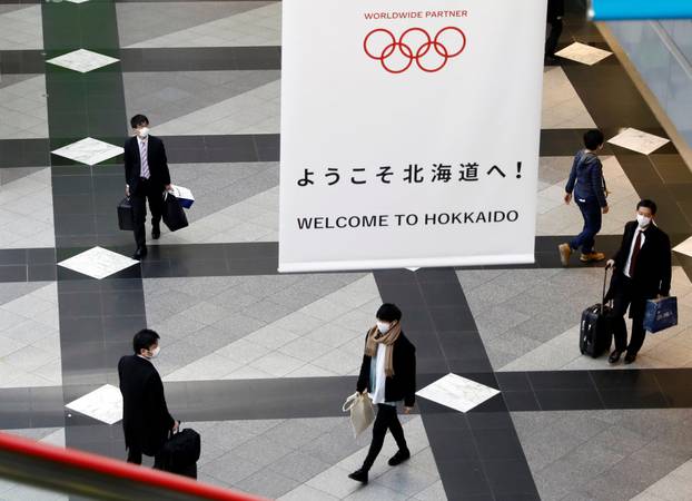 Passengers wearing protective face masks, following an outbreak of the coronavirus, walk under a campaign banner for Tokyo 2020 Olympic Games at New Chitose Airport in Chitose, Hokkaido