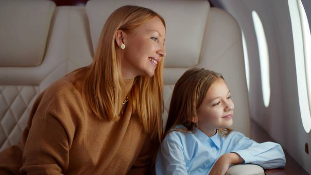 Mature elegant mother and preteen daughter looking through window flying on airplane