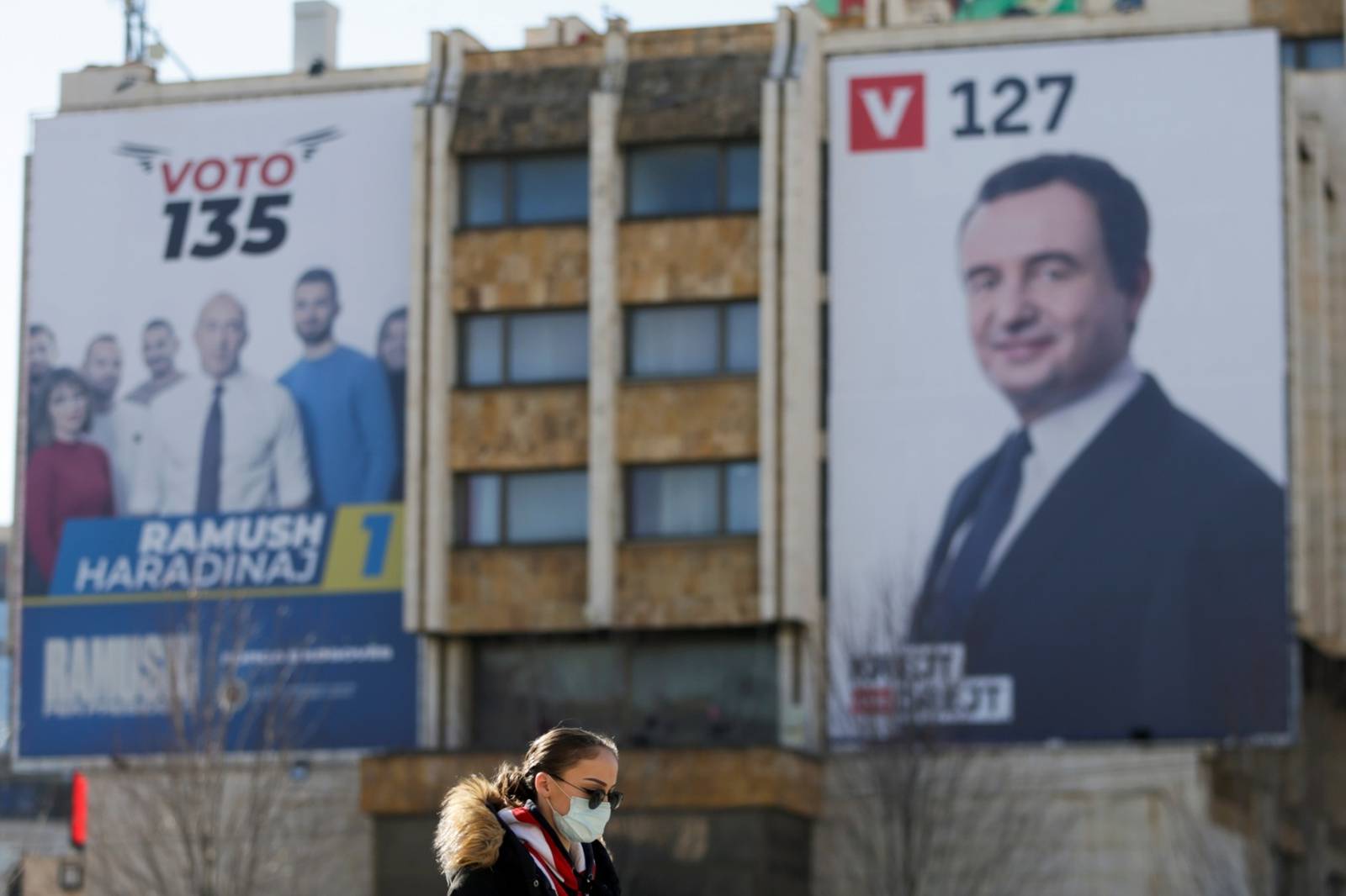 Woman wearing a mask walks near electoral campaign billboards in Pristina