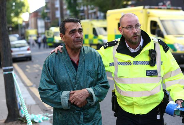 A police officer helps to evacuate a local resident from close to the scene of a serious fire in a tower block at Latimer Road in West London