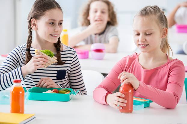 Pogled sprijeda na dvije mlađe djevojčice u školskoj kantini za vrijeme ručka
