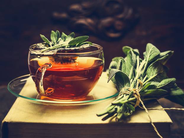 Herbal tea made from sage in glass cup standing on books, nearby