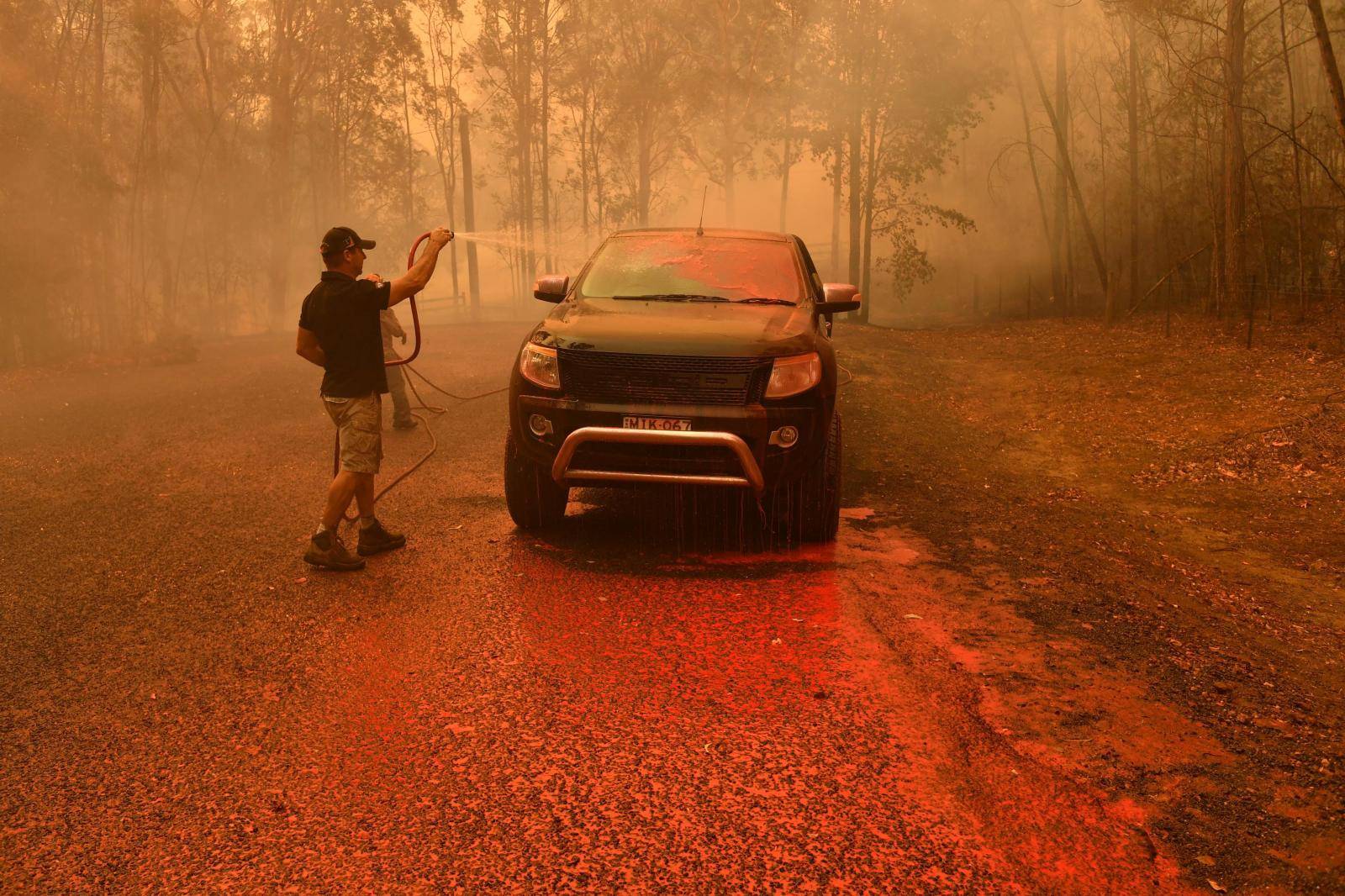 A local man hoses down fire retardant during a bushfire in Werombi, 50 km southwest of Sydney