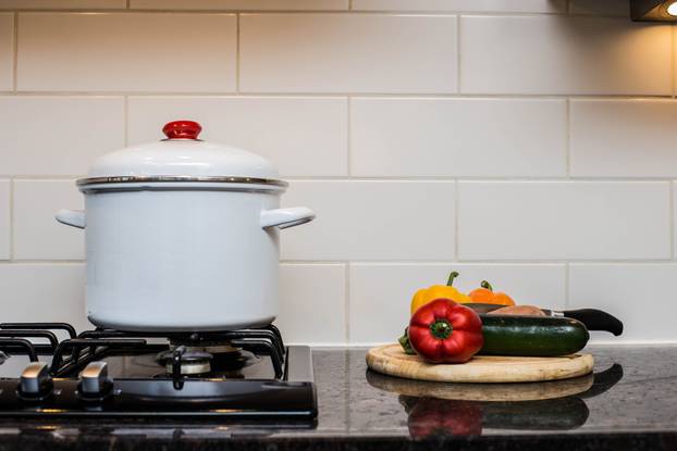 A large stock pot on a stove with vegetables cut for making soup