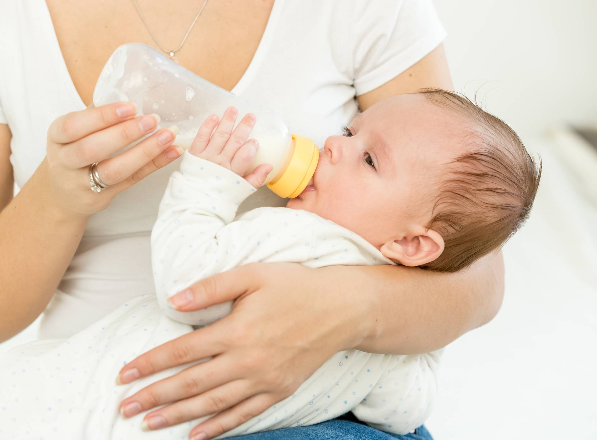 Mother giving milk from bottle to her baby sleeping on hands