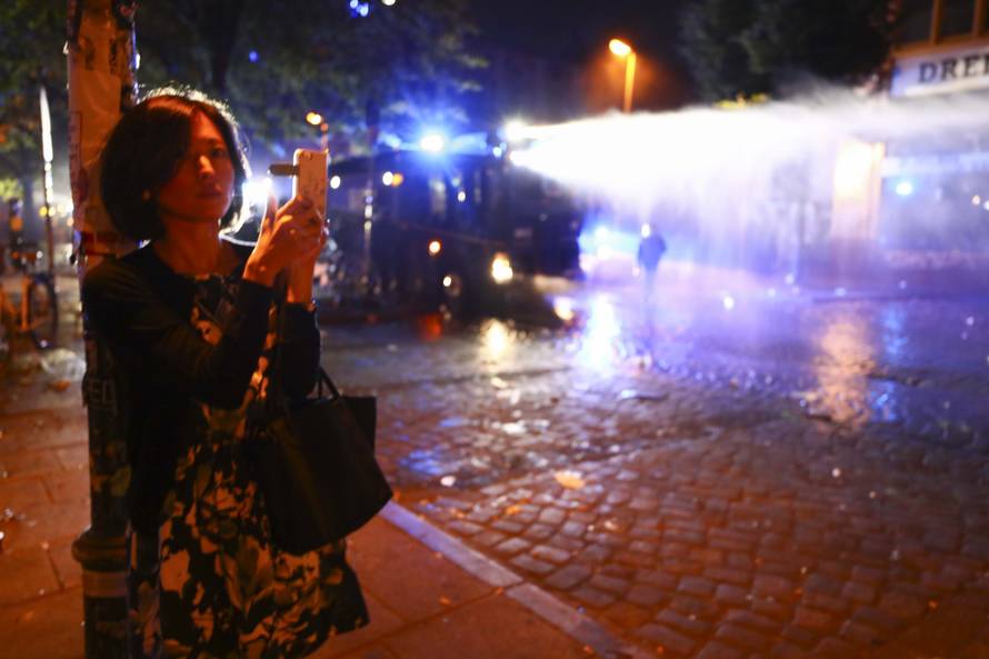 A woman takes pictures as riot police uses water cannons against protesters during demonstrations at the G20 summit in Hamburg