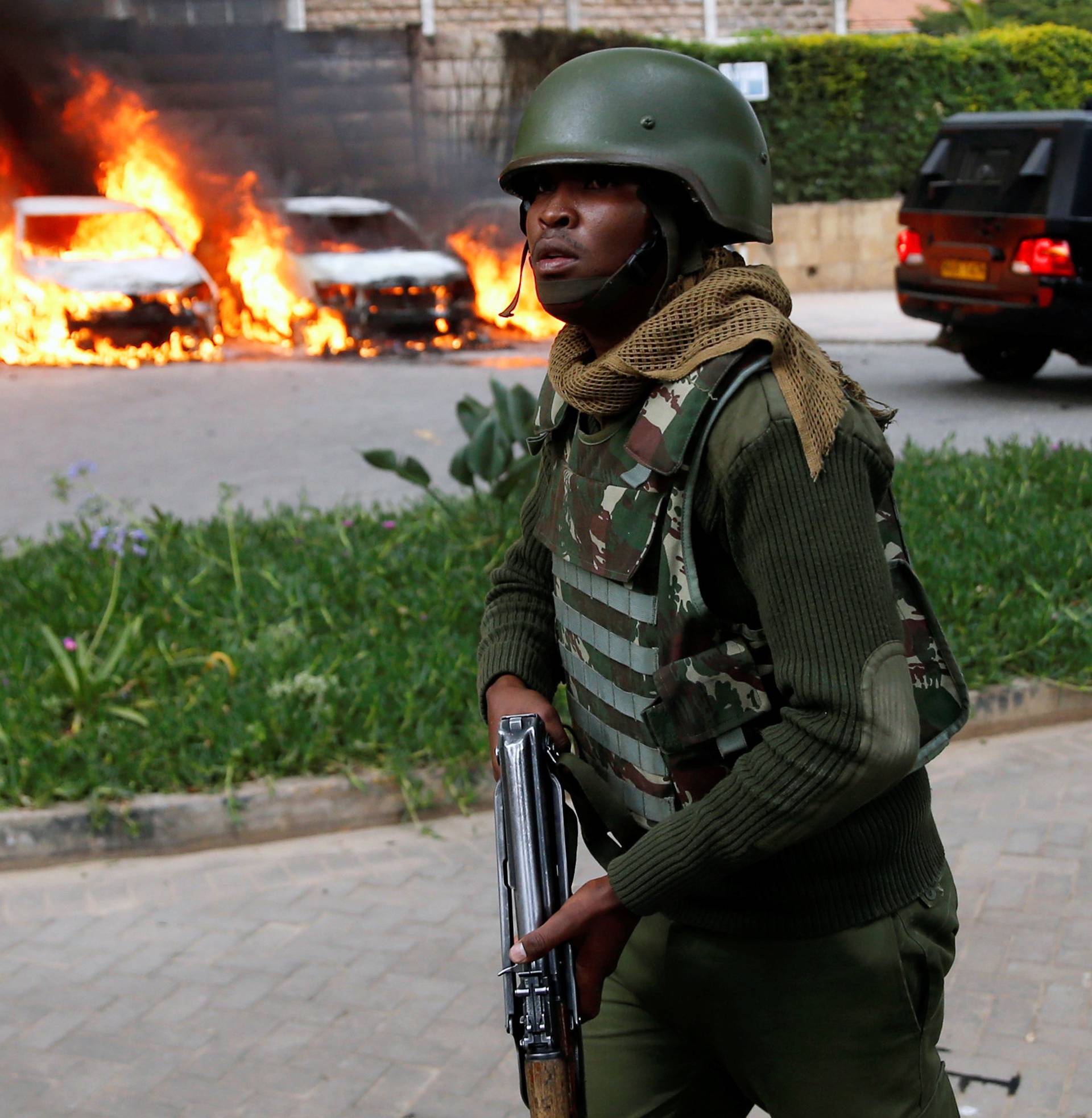 A policeman runs past burning cars at the scene where explosions and gunshots were heard at the Dusit hotel compound, in Nairobi