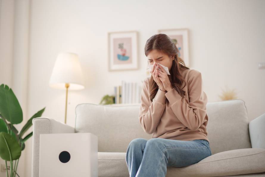Young,Asian,Woman,Sits,On,A,Couch,,Sneezing,And,Holding