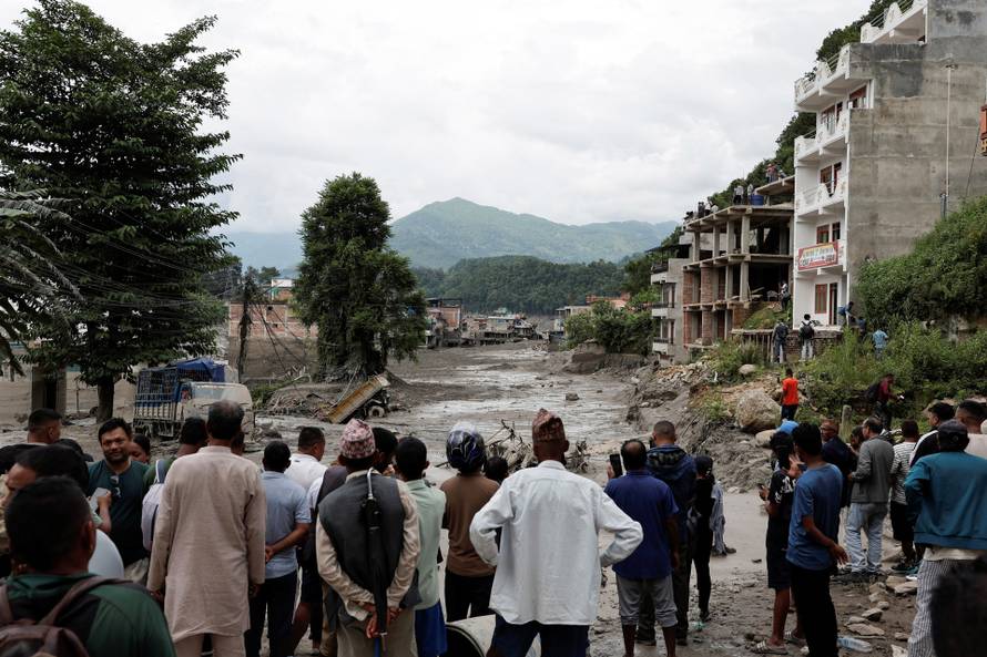 People stand near mud covered houses and a road, following a flash flood at Trishuli, Nepal