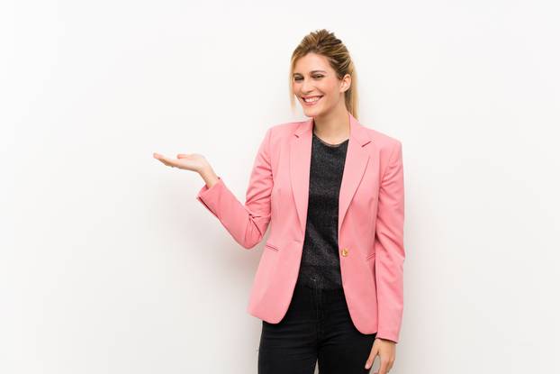 Young blonde woman with pink suit holding copyspace imaginary on the palm to insert an ad