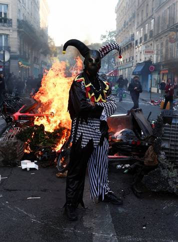 A demonstrator wearing a costume stands in front of burning flames, in Paris