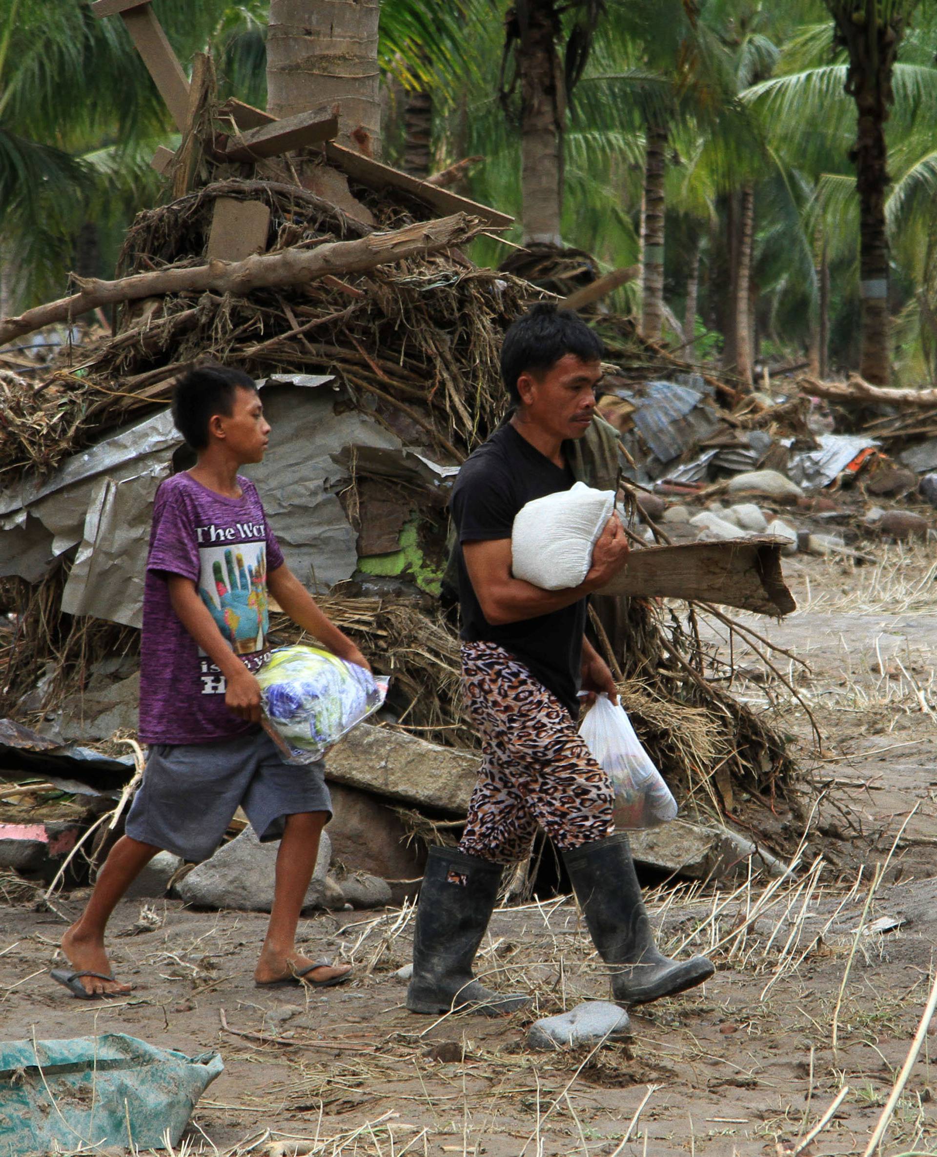 Residents carry relief goods past debris in a village devastated by flash floods in Salvador, Lanao del Norte