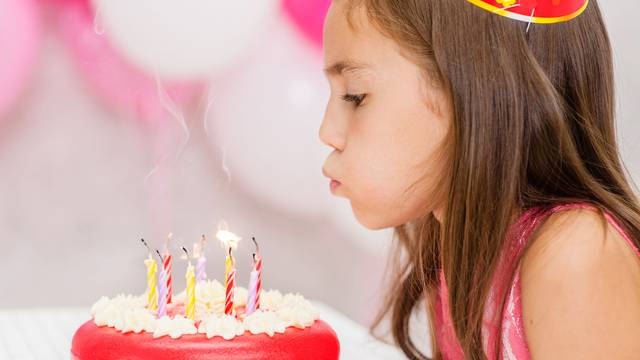 Cute girl celebrating his birthday and blowing candles on cake