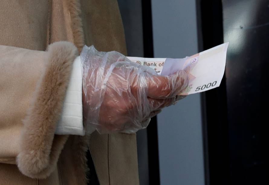 A woman wearing a plastic glove holds money as she stands in a queue to buy face masks amid the rise in confirmed cases of the novel coronavirus in Daegu