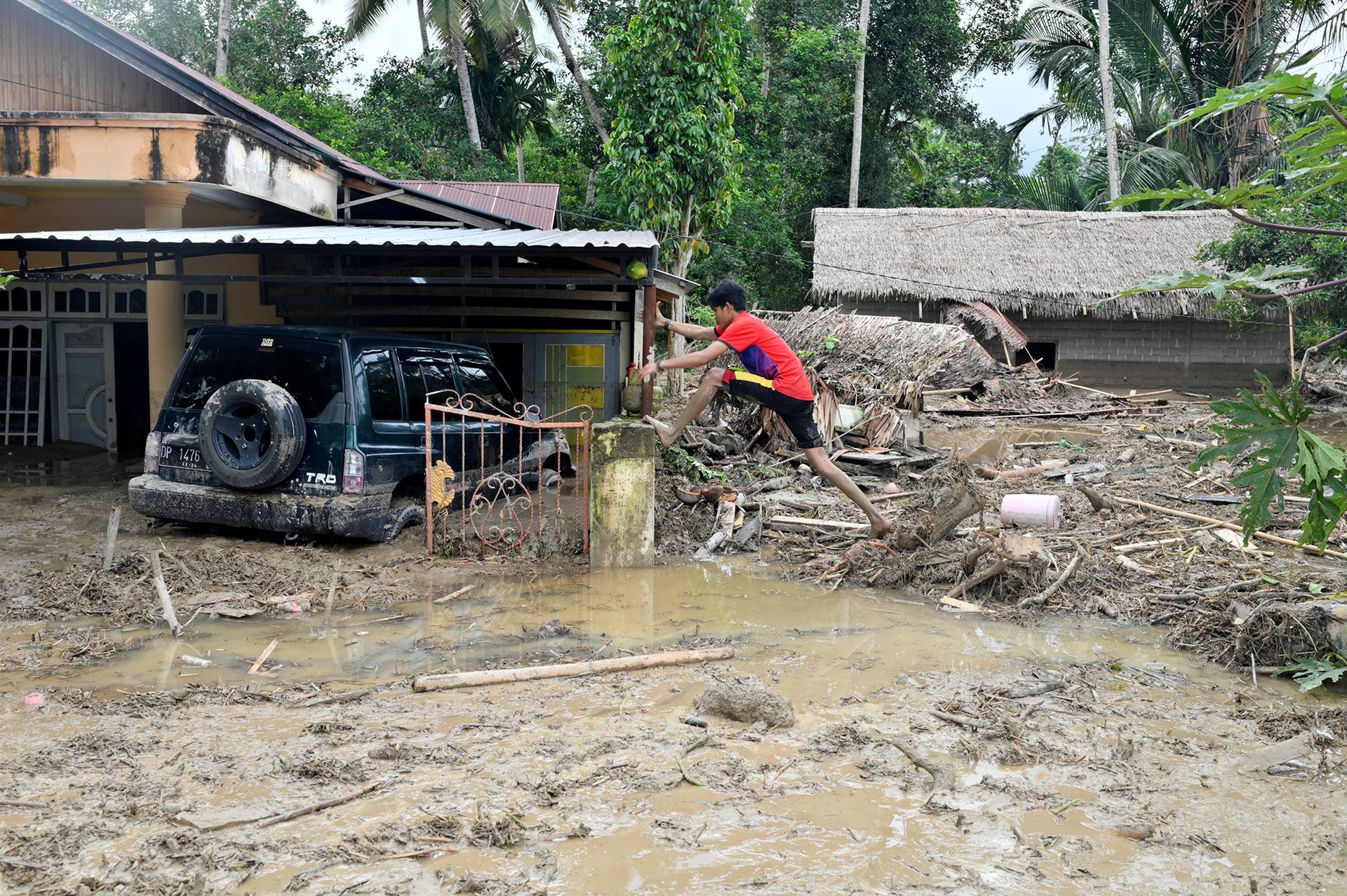 A man steps over debris near a house submerged in mud after flash floods swept through Radda village, as several people were killed and dozens remain missing in North Luwu, Sulawesi