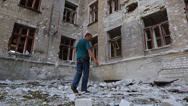 Local resident Andrey Butenko stands in front of the damaged school building where he lives in the basement in Lysychansk