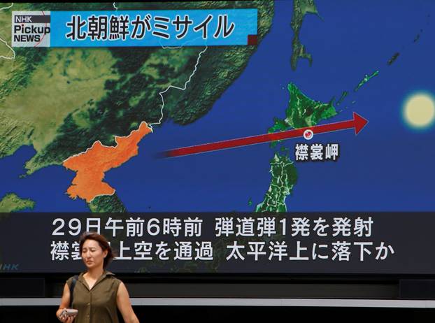 A woman walks past a large TV screen showing news about North Korea