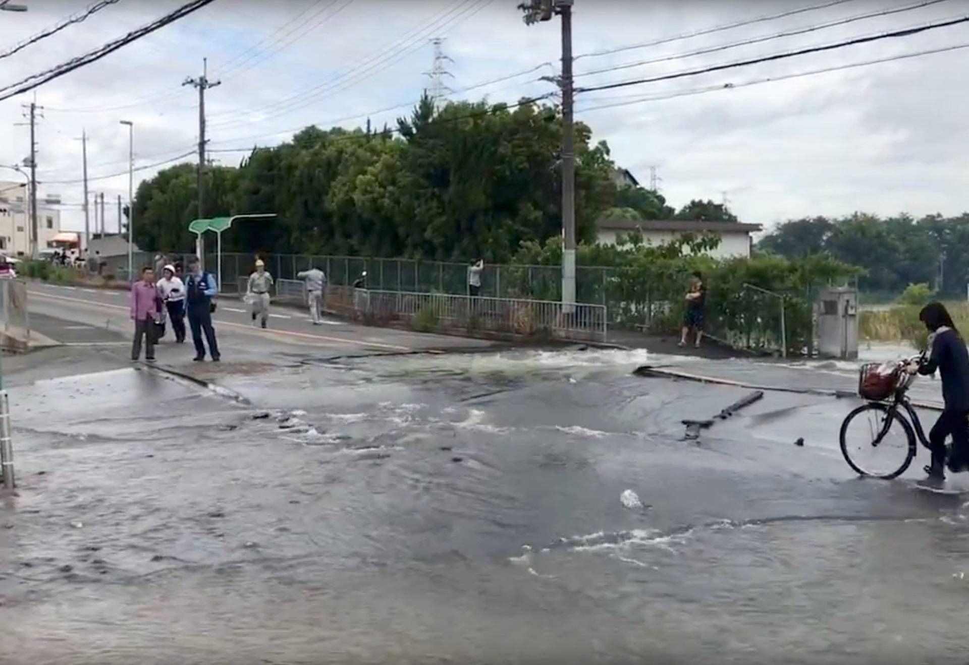 People stand at a flooded road damaged after an earthquake hit Osaka