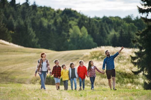 Group of school children with teacher on field trip in nature, walking.
