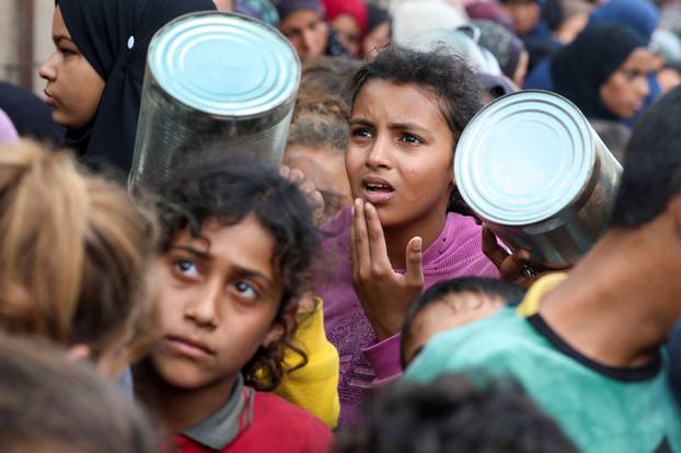 Palestinians gather to receive meals cooked by a charity kitchen, in Deir Al-Balah, central Gaza Strip