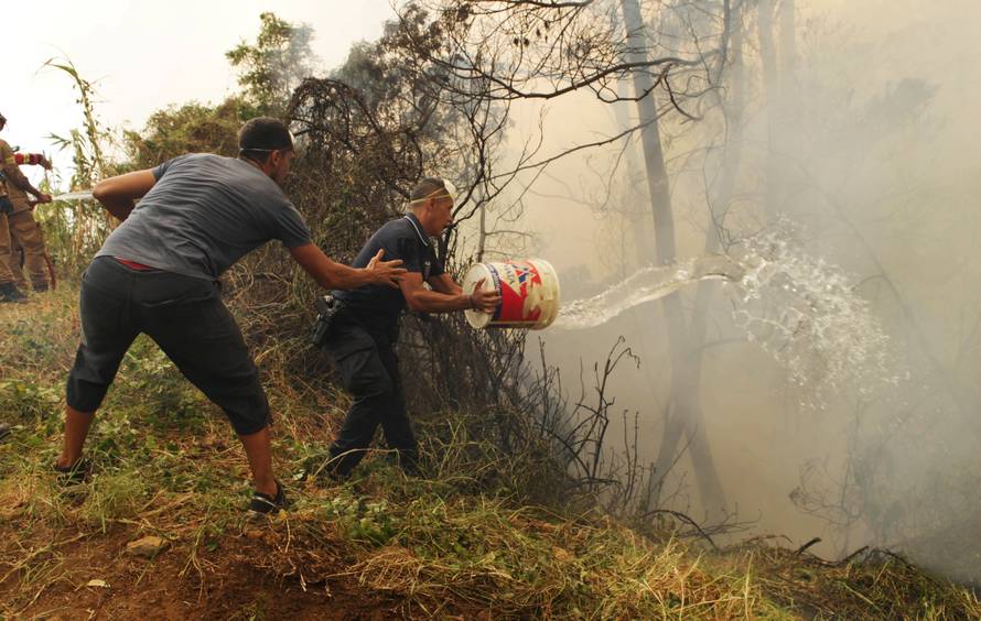 Civilians, and police officers use water buckets to help extinguish a forest fire near houses at Sao Joao Latrao, Funchal, Madeira island