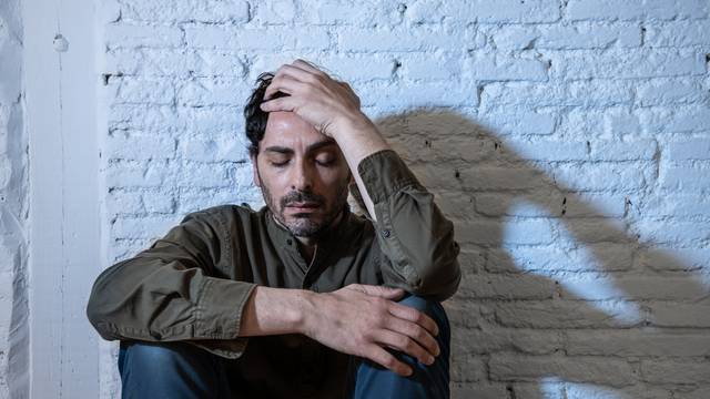 sad depressed man leaning against a wall in mental health concept