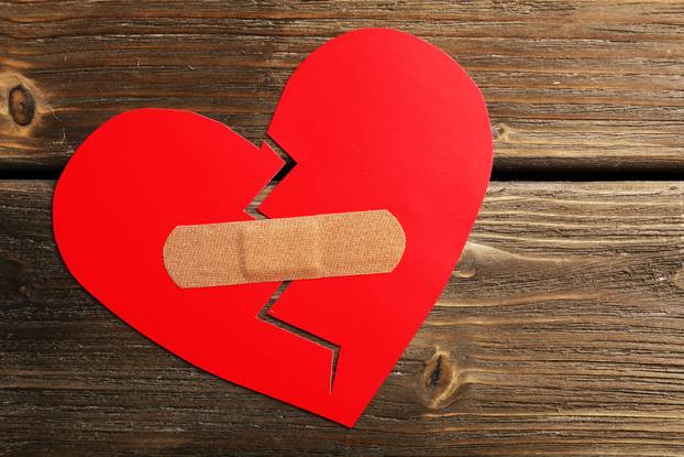 Broken heart with plaster on wooden background