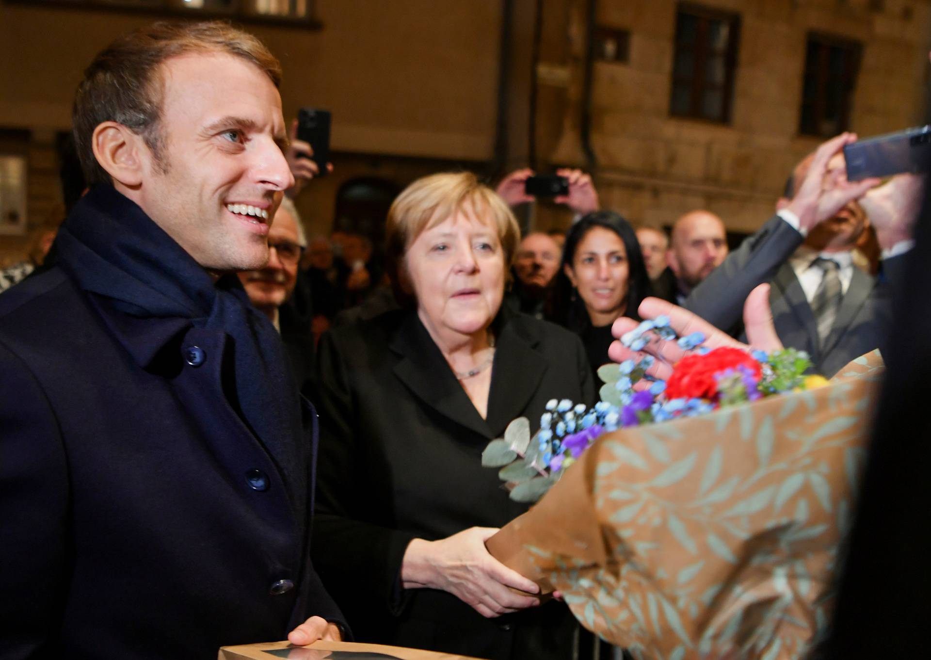 Outgoing German Chancellor Angela Merkel and France's President Emmanuel Macron receive flowers and a bottle of wine as gifts upon their arrival for talks, in Beaune